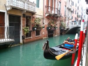 Vista de cerca de una góndola negra tradicional amarrada en un pintoresco y estrecho canal de Venecia, Italia, rodeado de históricos edificios de ladrillo y un pequeño puente peatonal. Manténgase conectado sin esfuerzo durante su escapada romántica a Venecia con la eSIM premium de SimpleSIM.