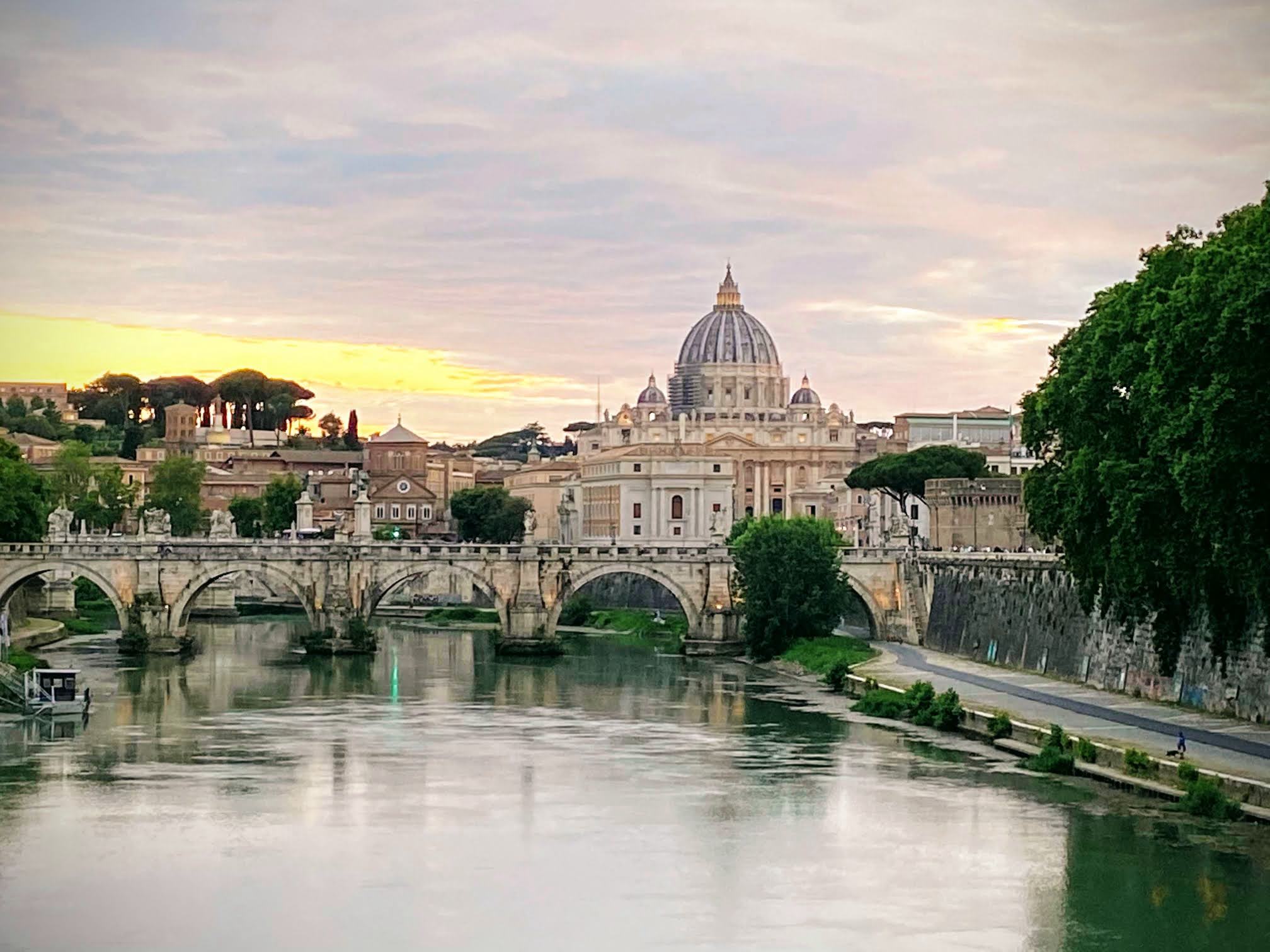 Impresionante puesta de sol con la cúpula de la Basílica de San Pedro y el Puente Sant'Angelo reflejándose en el río Tíber en Roma, Italia. Cobertura eSIM ininterrumpida para viajeros internacionales en toda Italia con SimpleSIM.