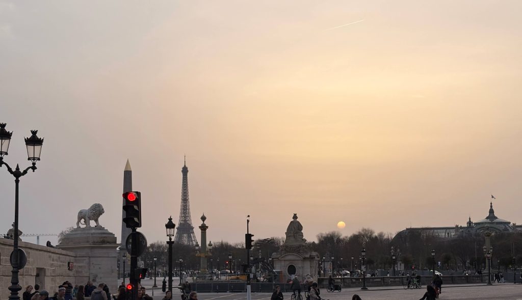 Coucher de soleil doré sur la place de la Concorde à Paris, avec l'obélisque au premier plan et la tour Eiffel se détachant sur un ciel orangé et violet.