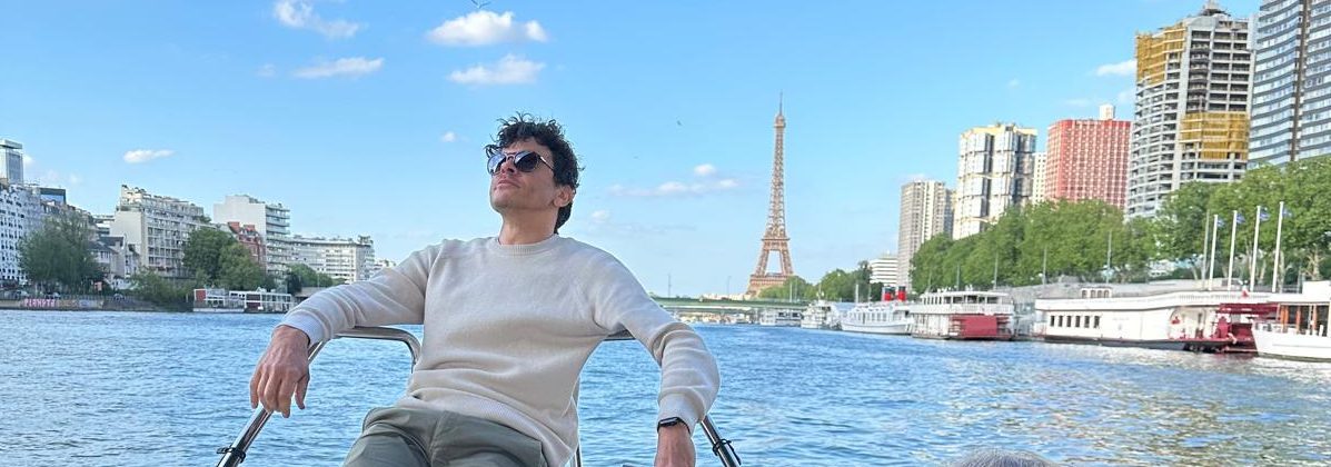 Des touristes profitent d'une promenade en bateau sur la Seine à Paris, avec la tour Eiffel en arrière-plan, par une journée ensoleillée.