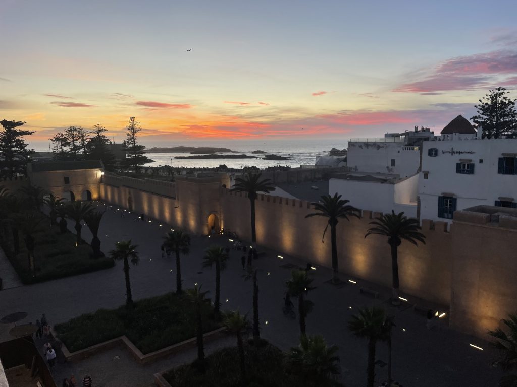 Die historischen Stadtmauern von Essaouira, im Abendrot beleuchtet von Palmen und mit Blick auf den Atlantischen Ozean in Marokko